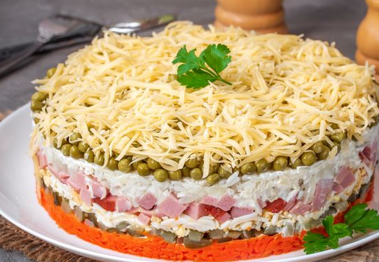 Layered salad with ham, carrots, rice and pickled cucumbers